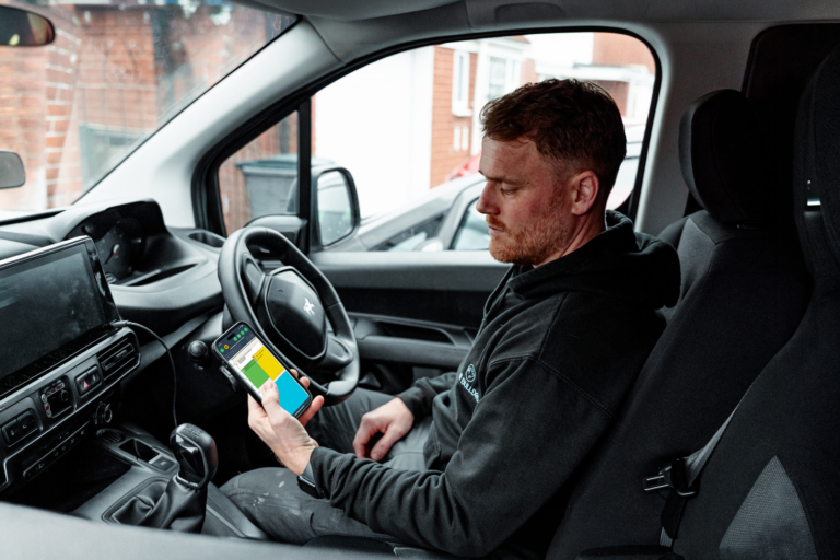 A tradesperson in the driver's seat, checking the diary on his phone