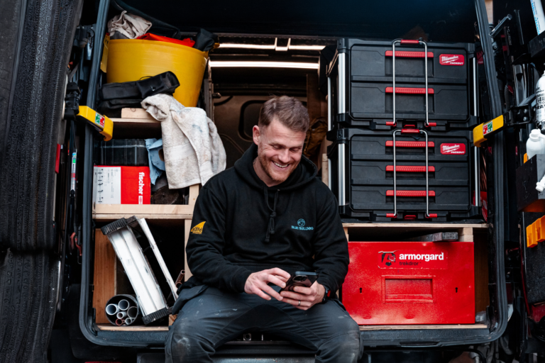A tradesperson sat in the back of his van, sending a quote from his phone